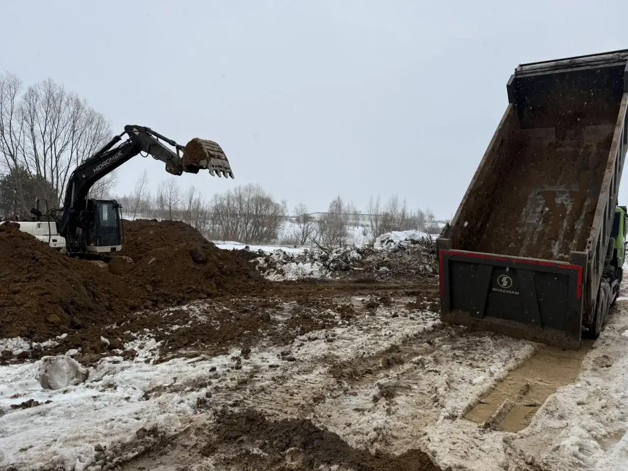 Экскаватор загружает грунт рядом с самосвалом